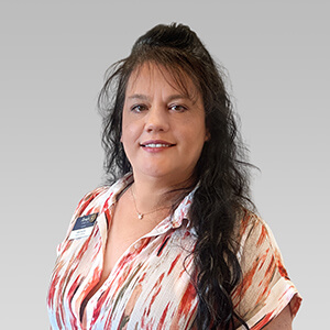 Person with long dark hair in white and red patterned shirt, gray background.