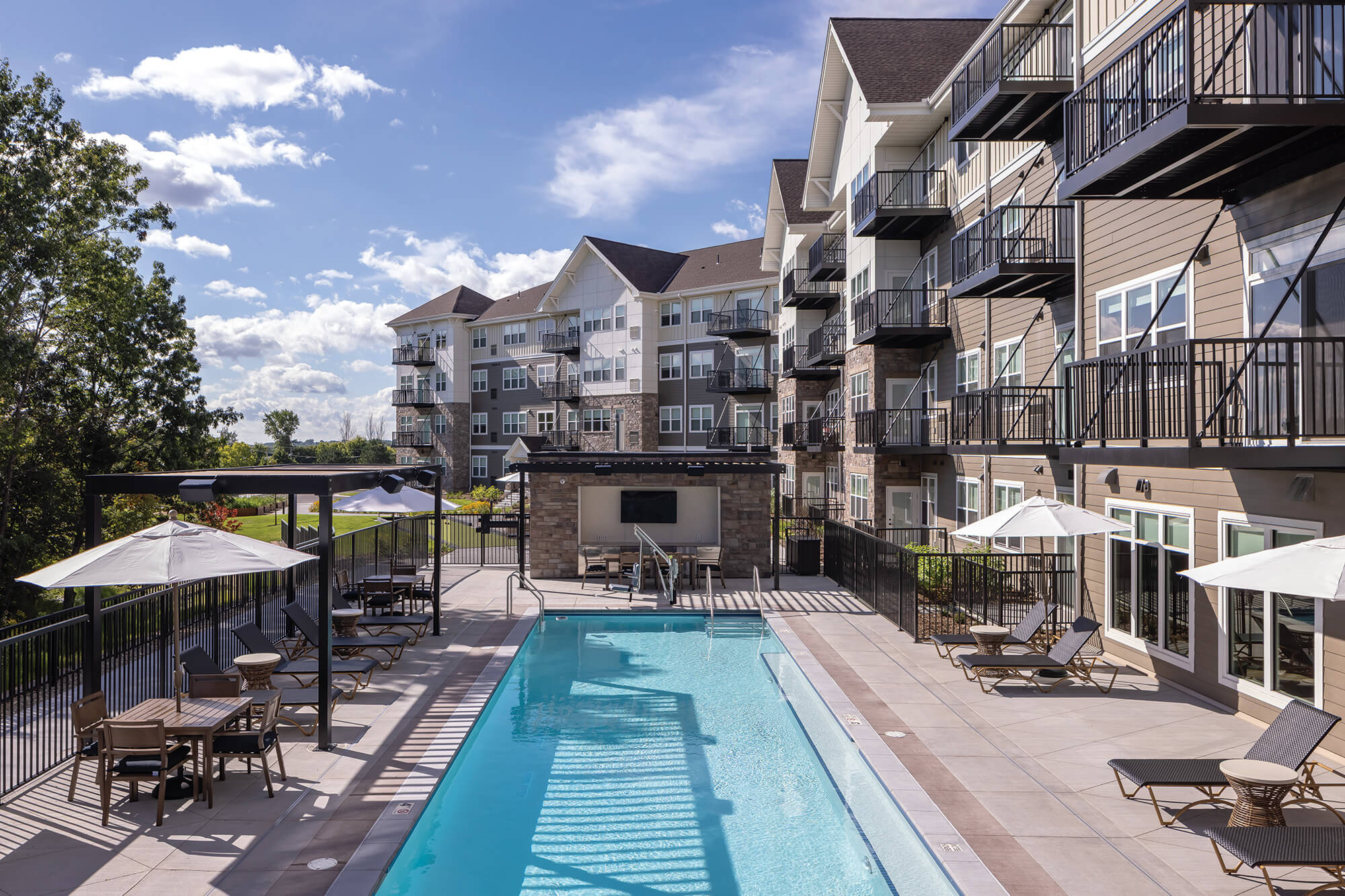 Modern senior living apartments with balconies, pool, and sun loungers under blue sky.