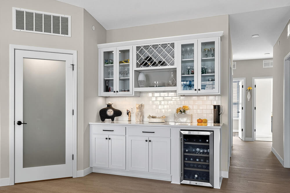 Modern white kitchen with glass cabinets, wine rack, and small fridge.