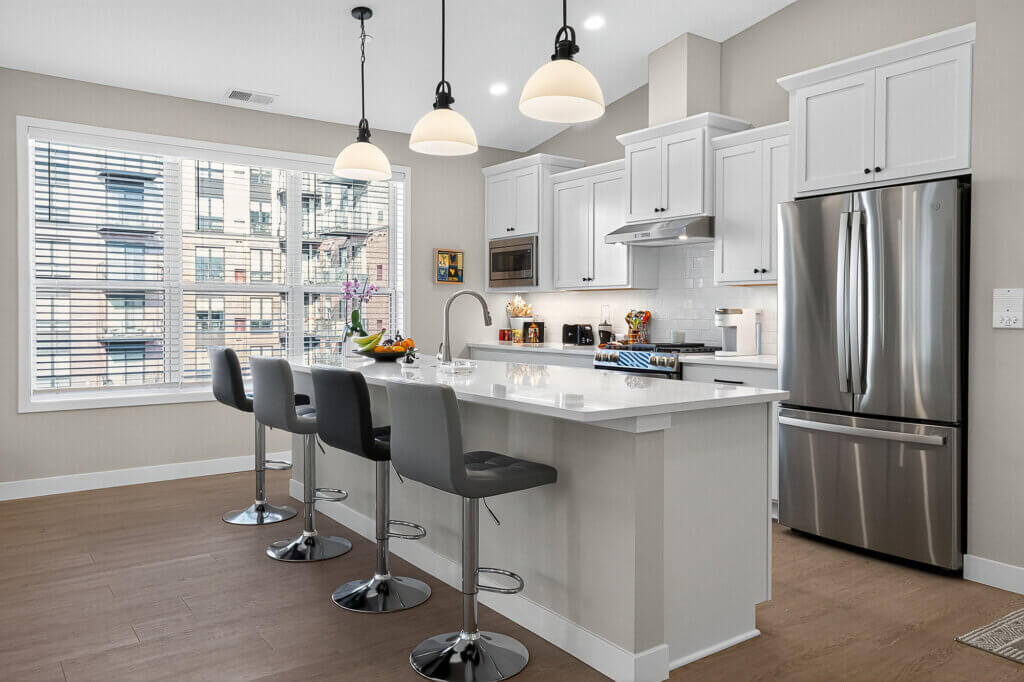 Modern kitchen with white cabinets, stainless steel appliances, and gray bar stools.