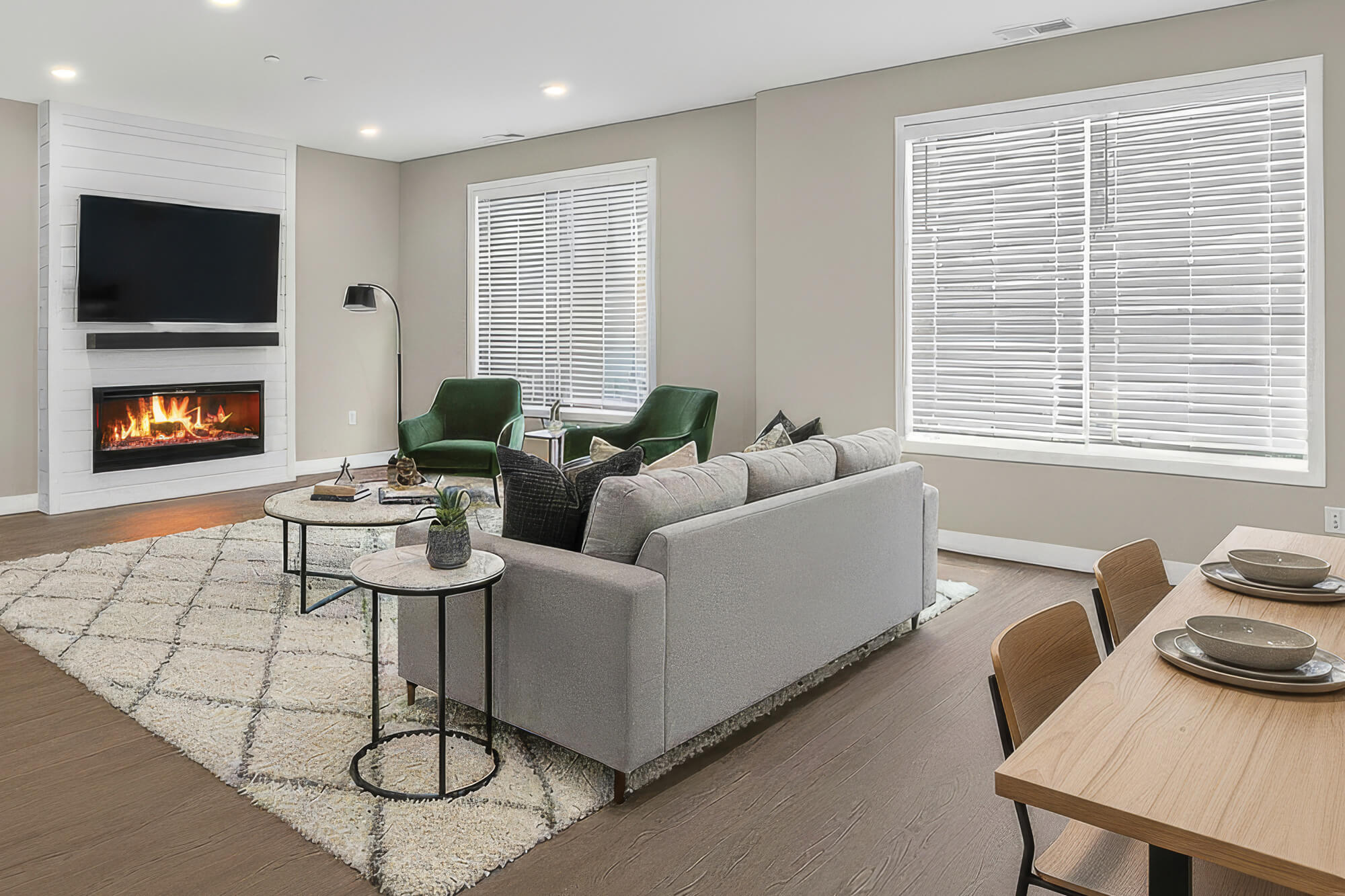 Modern living room with gray couch, green chairs, fireplace, and large windows.