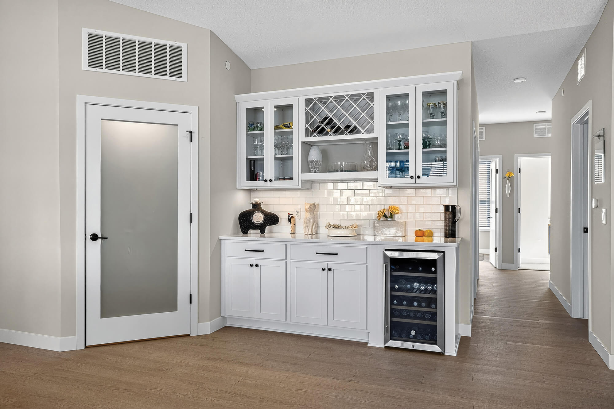 Stylish white wine bar area with glass cabinets and wine cooler, in a modern setting.
