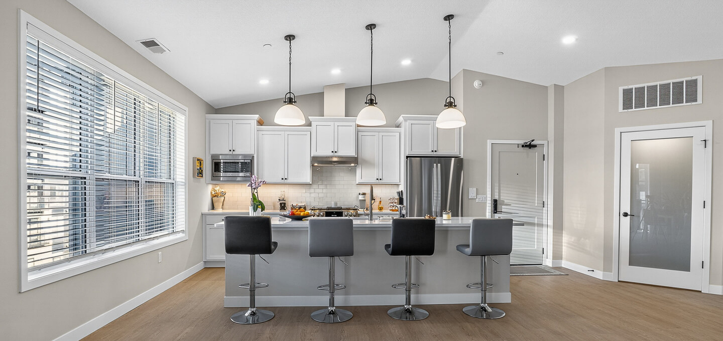 Modern kitchen with white cabinets, gray chairs, and hanging pendant lights.